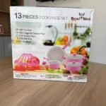 Pack de 13 piezas de cookware Royal Mark en caja blanca con de sartén, ollas y utensilios rosados sobre mesa de madera.