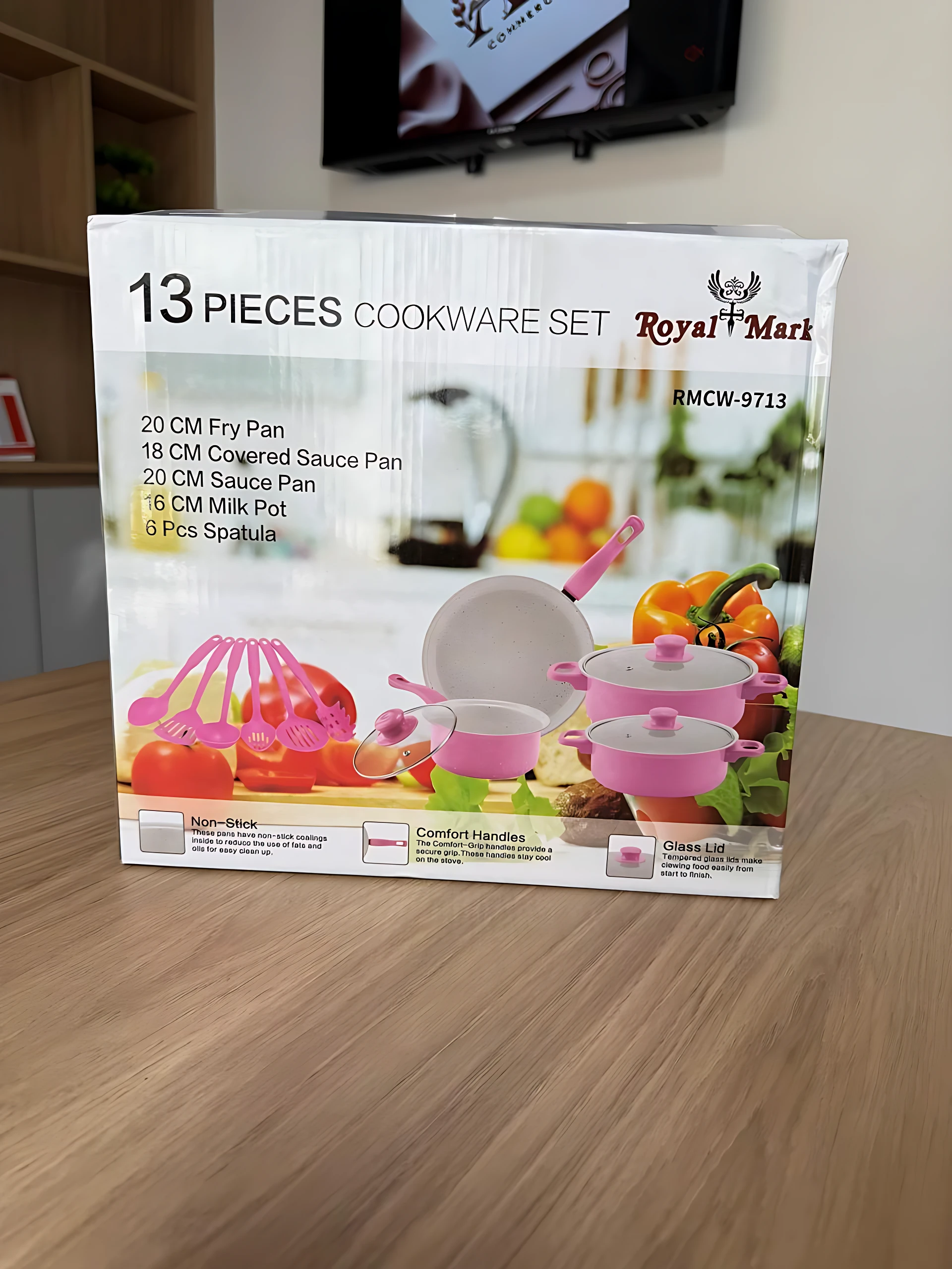Pack de 13 piezas de cookware Royal Mark en caja blanca con de sartén, ollas y utensilios rosados sobre mesa de madera.