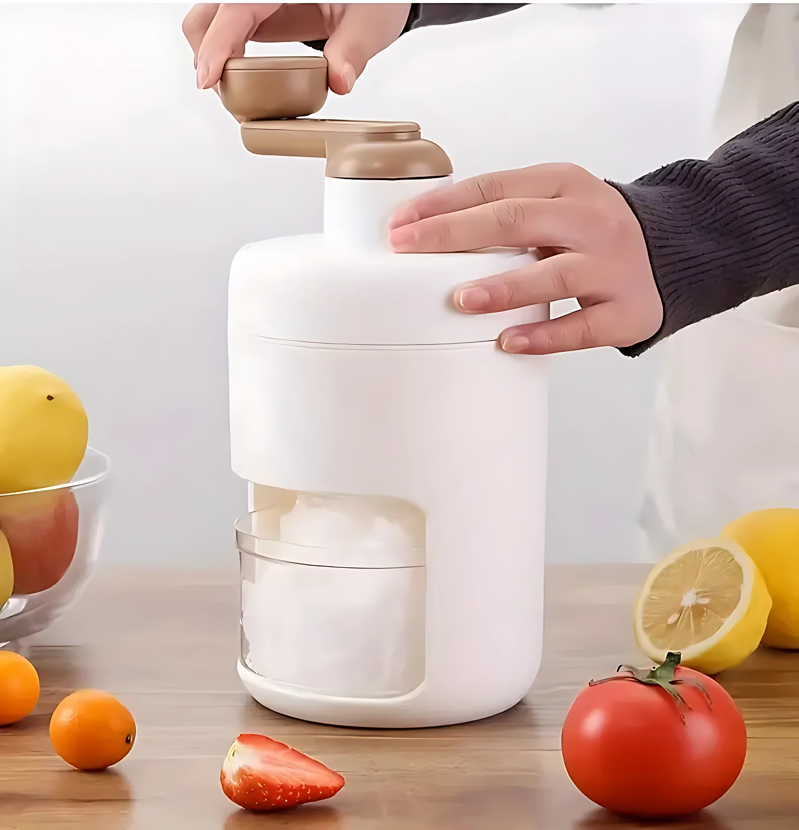 Picador de hielo manual blanco con manivela beige. Se observa la acción de triturar hielo a través de una ventana lateral. El dispositivo descansa sobre una mesa rodeado de frutas frescas como limones y fresas.
