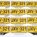 Set de dos porta placas de acero inoxidable para motos, con diseño amarillo y negro, mostrando matrículas colombianas JXV-322.