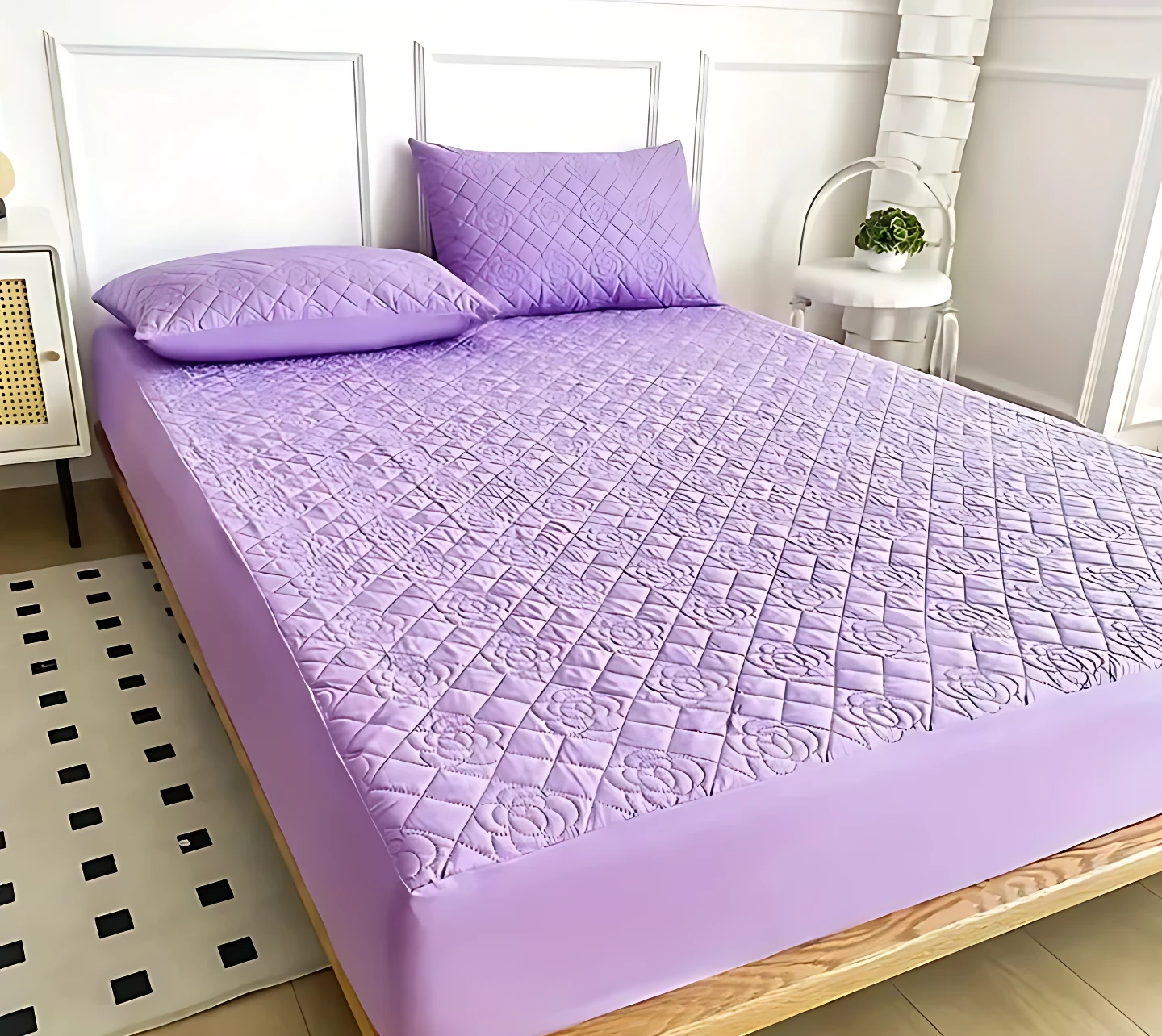 Protector de colchón acolchado color lila con patrón de rombos y relieve floral. Vista cenital sobre cama con dos almohadas del mismo tono y textura suave.