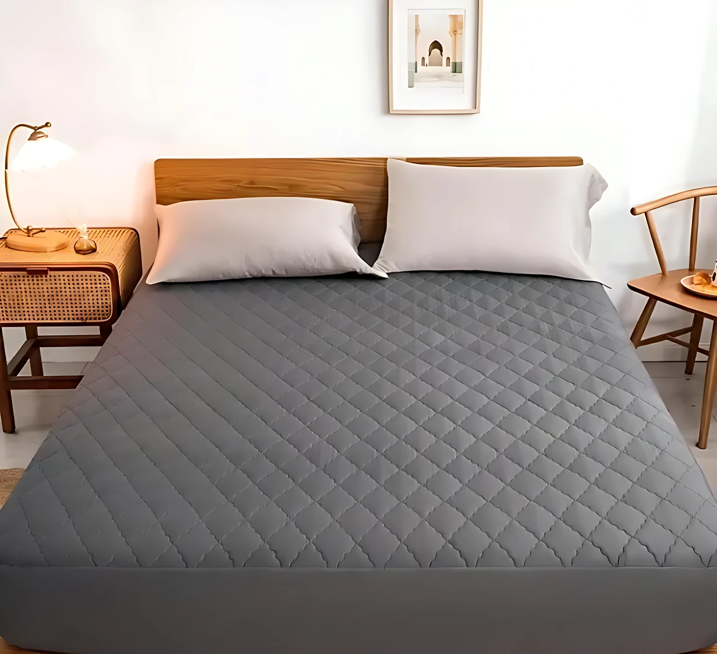 Protector de colchón antifluido color gris con textura acolchada en rombos, exhibido en cama con cabecero de madera y almohadas blancas.