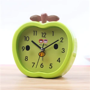 Reloj despertador verde en forma de manzana con manecillas negras y dos caritas sonrientes.