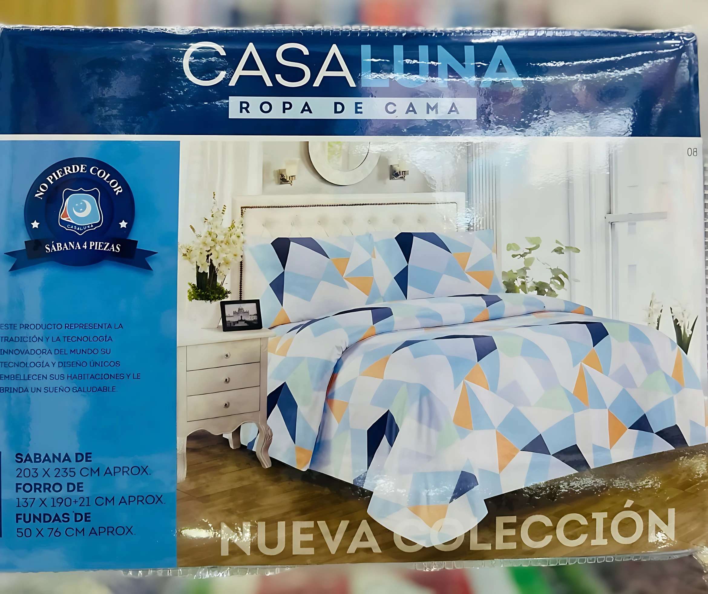 Paquete de sábanas Casaluna mostrando cama con diseño geométrico en triángulos azules y naranjas. Se leen las medidas de 203 x 235 cm en la caja.