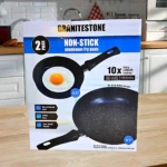 Caja de set de dos sartenes antiadherentes Granitestone de aluminio. Una de 5.5 pulgadas con huevo y otra de 9.5 pulgadas vacía, negras con puntas blancas sobre encimera
