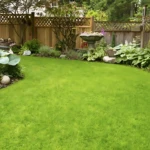 Césped verde vibrante en jardín con flores variadas y cercado de madera.