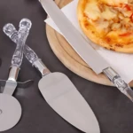 Set de tres utensilios de cocina con mangos acrílicos transparentes: cuchillo serrado para pizza, espátula de servir y rodillo cortador. Incluyen base metálica y mango ergonómico.