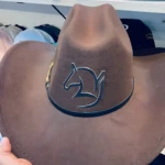 Sombrero café estilo vaquero con estampado de caballo, banda negra y hebilla dorada.