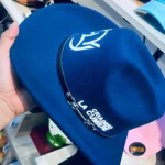 Sombrero azul de algodón estampado "Criadero La Cumbre" con logo blanco, sostenido por mano.
