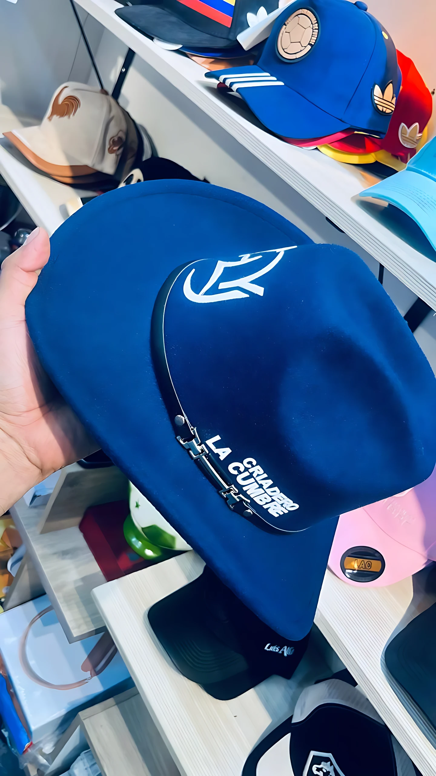 Sombrero azul de algodón estampado "Criadero La Cumbre" con logo blanco, sostenido por mano.