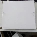 Caja blanca rectangular de la pistola de puntadas Stitchy, vista superior sobre escritorio con accesorios de gaming al fondo.