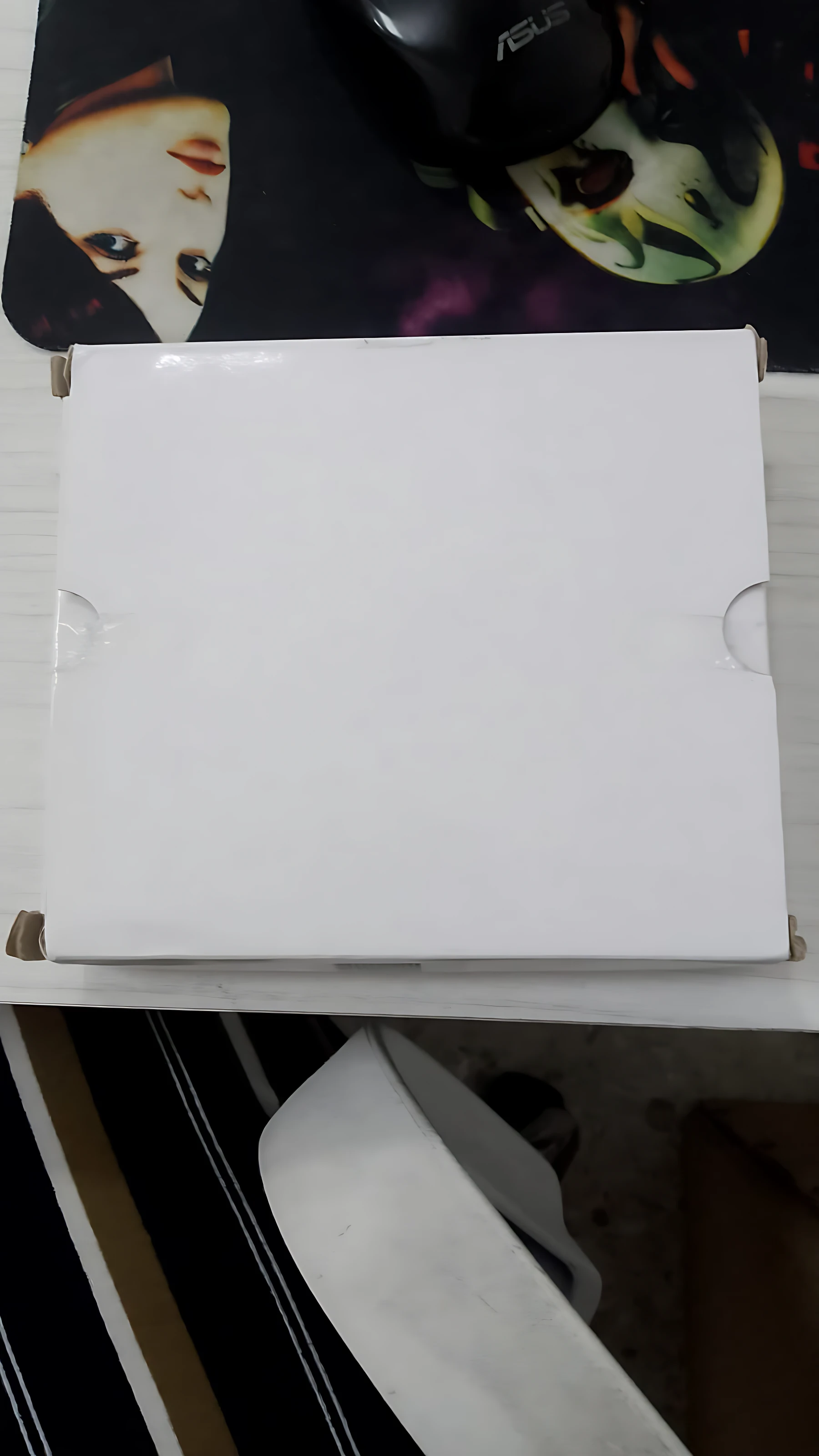 Caja blanca rectangular de la pistola de puntadas Stitchy, vista superior sobre escritorio con accesorios de gaming al fondo.