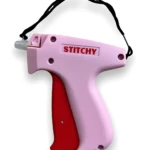 Pistola de puntadas Stitchy en color rosa con mango rojo, diseño ergonómico y asa negra para transporte.