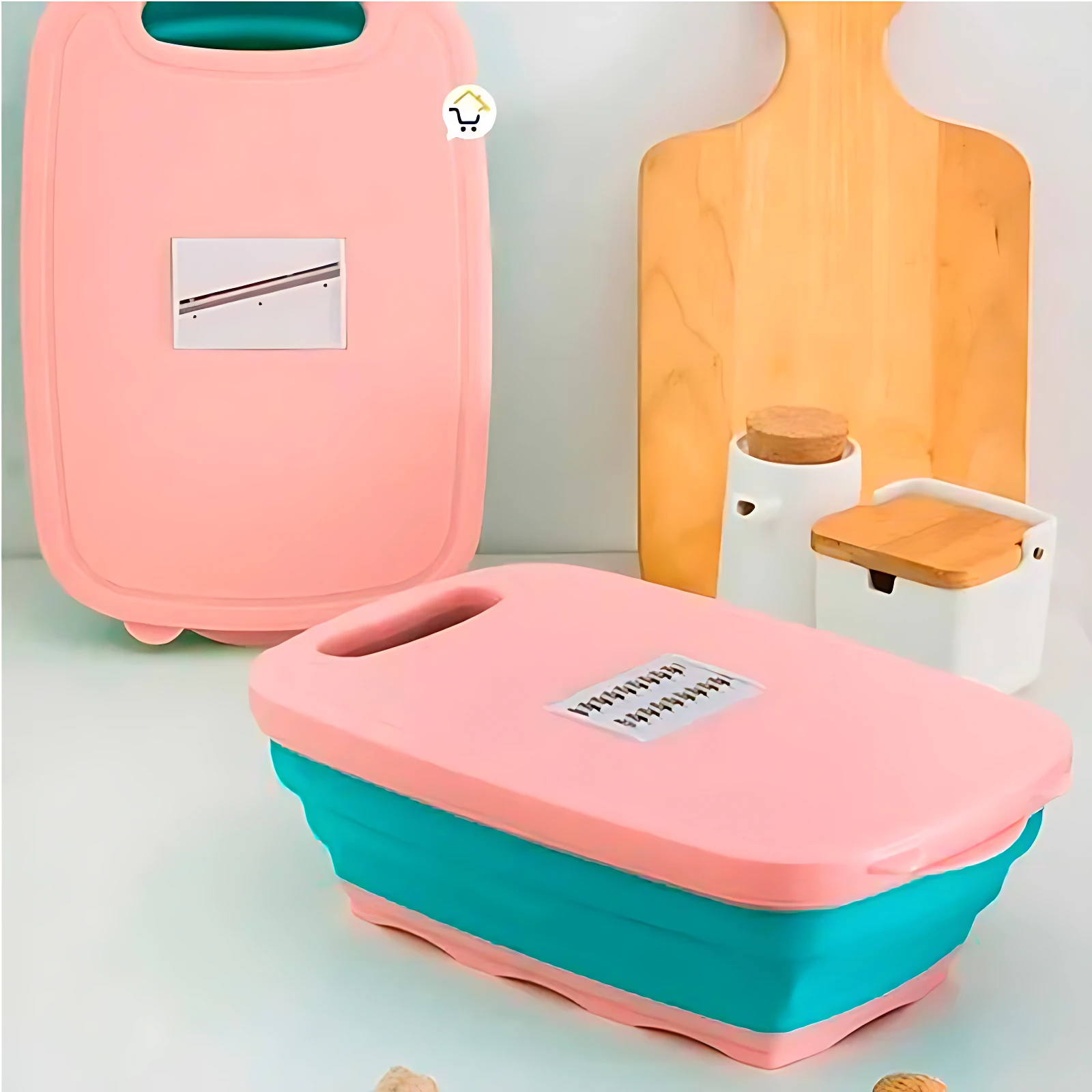 Tabla de cortar plegable en rosa y turquesa con colador integrado y cinco cuchillas intercambiables, mostrada abierta y cerrada sobre superficie blanca.