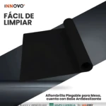 Tapete negro plegable para mesa con base antideslizante, enrollado parcialmente sobre superficie blanca.