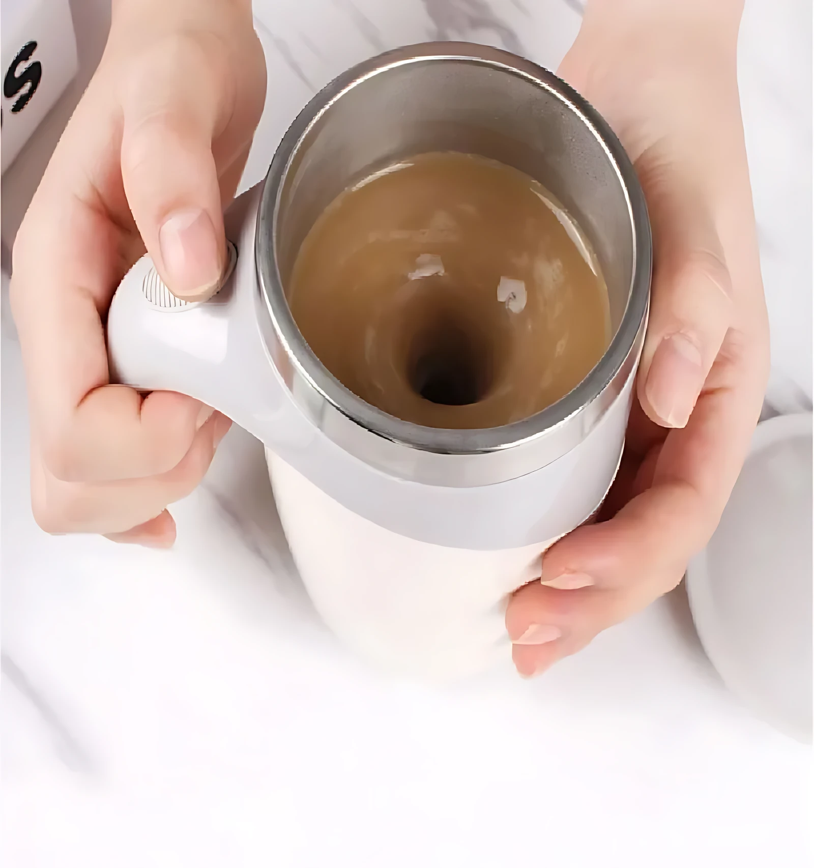 Taza mezcladora automática giratoria en color blanco, con líquido café en movimiento, sostenida por manos sobre superficie blanca.