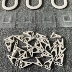 Tendedero plegable de plástico blanco con ganchos y base adhesiva, mostrando piezas desarmadas sobre superficie gris texturizada.