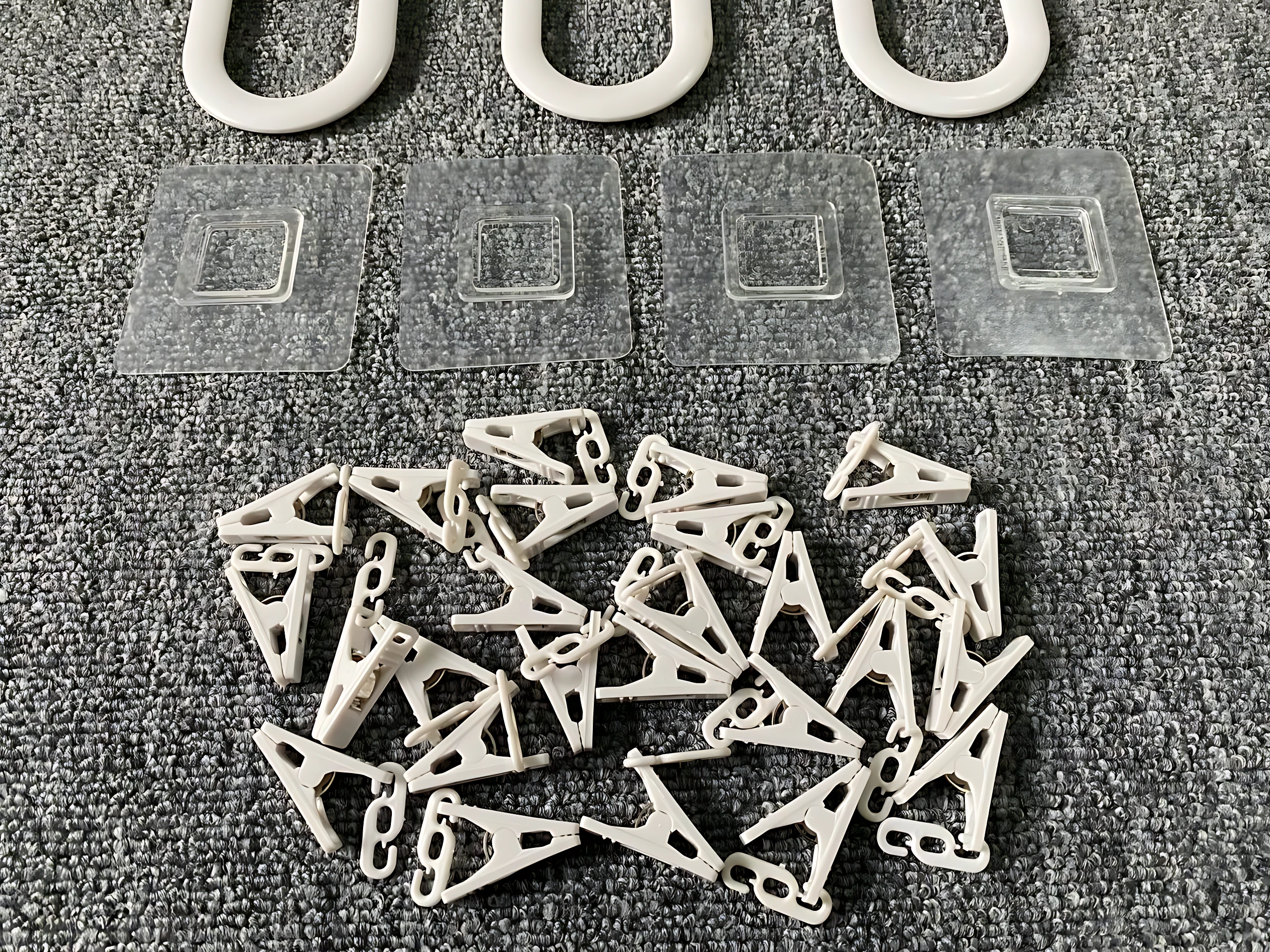 Tendedero plegable de plástico blanco con ganchos y base adhesiva, mostrando piezas desarmadas sobre superficie gris texturizada.