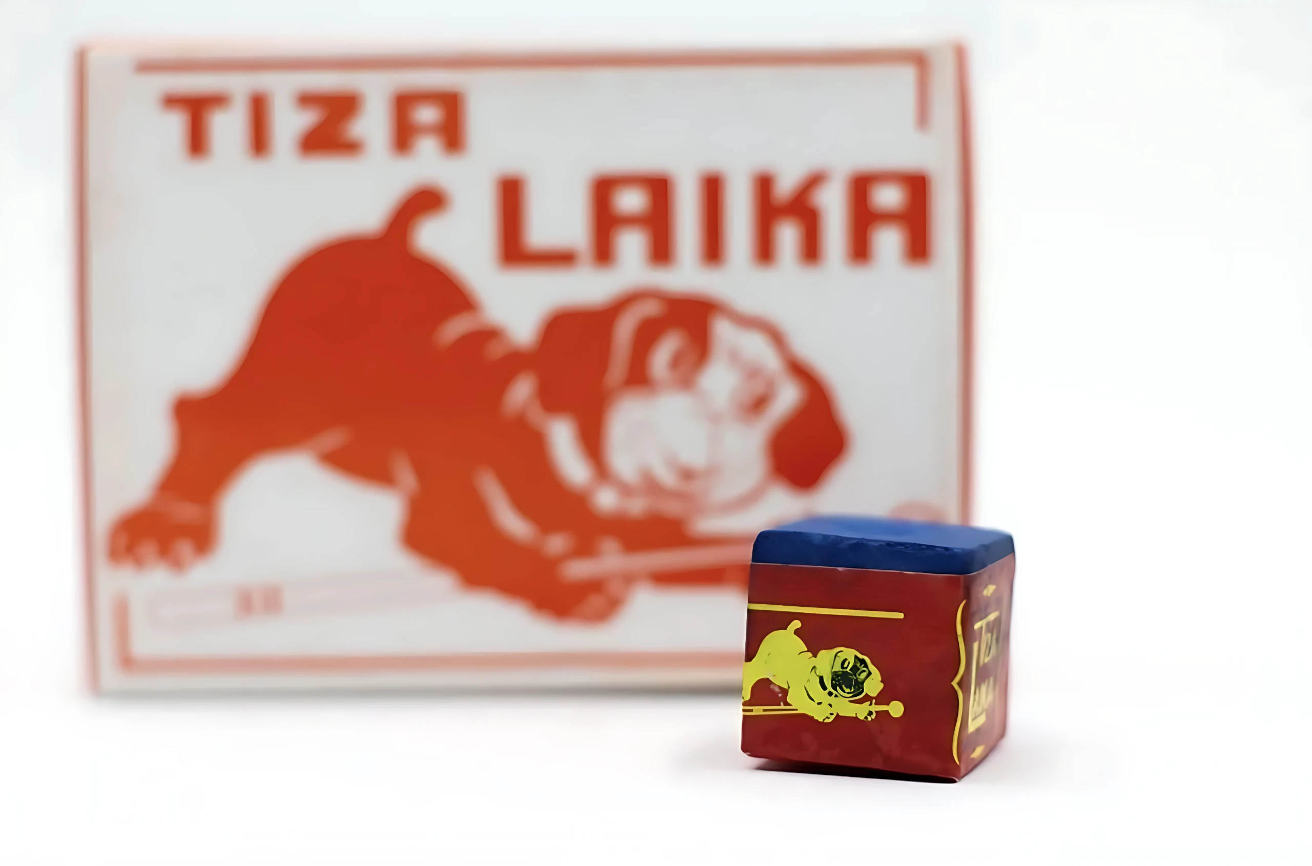 Cubo de tiza Laika para billar, color rojo con diseño de perro amarillo y tapa azul, junto a su caja con del mismo perro y texto Tiza Laika.