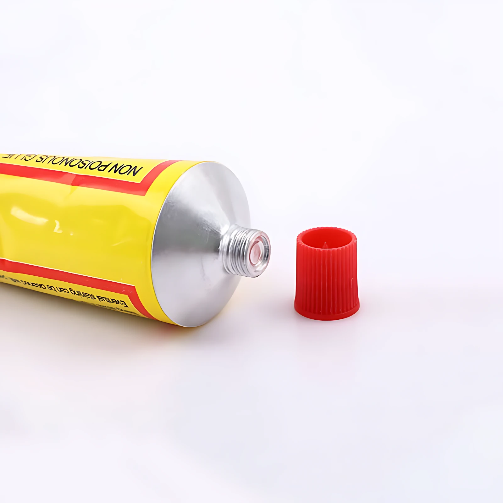 Tubo de pegamento plateado con tapa roja, etiqueta amarilla con texto "NON POISONOUS GLUE".
