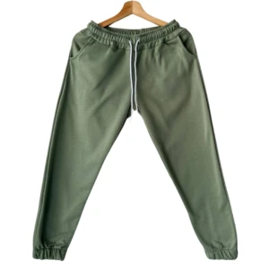 Jogger dama en verde manzana, con cintura elástica y cordón blanco, vista frontal colgada en perchero.