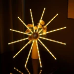 Lámpara LED estrella auditórica con 12 brazos giratorios, luces amarillas cálidas y centro decorativo con flores artificiales.