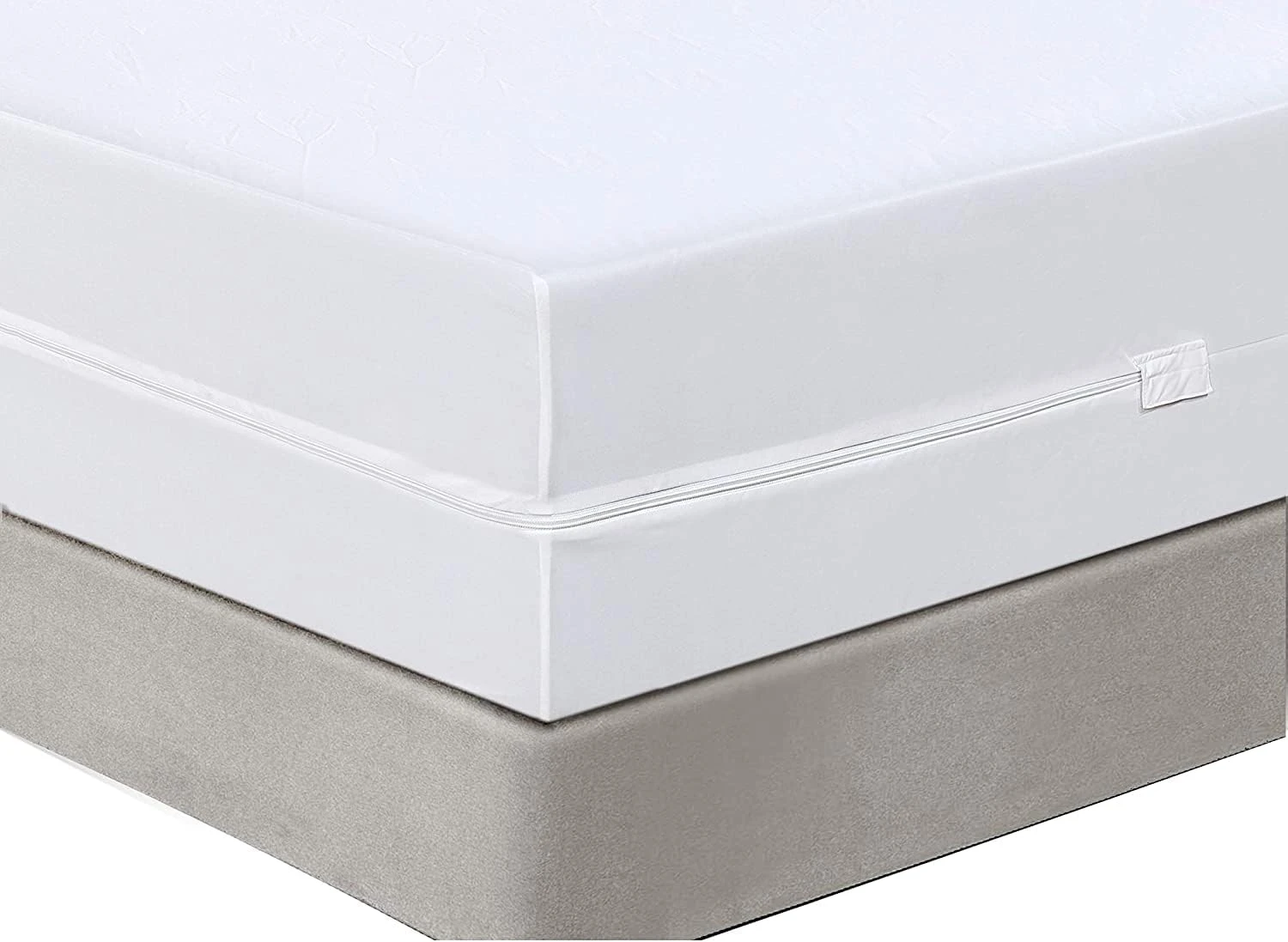 Protector colchón blanco con costura visible y cierre lateral, colocado sobre base de cama gris.