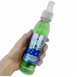 Botella de spray Hielo Mineral con Cannabis y Arnica, líquido verde translúcido, etiqueta azul con de cristales, mano sosteniendo el envase en ángulo lateral.