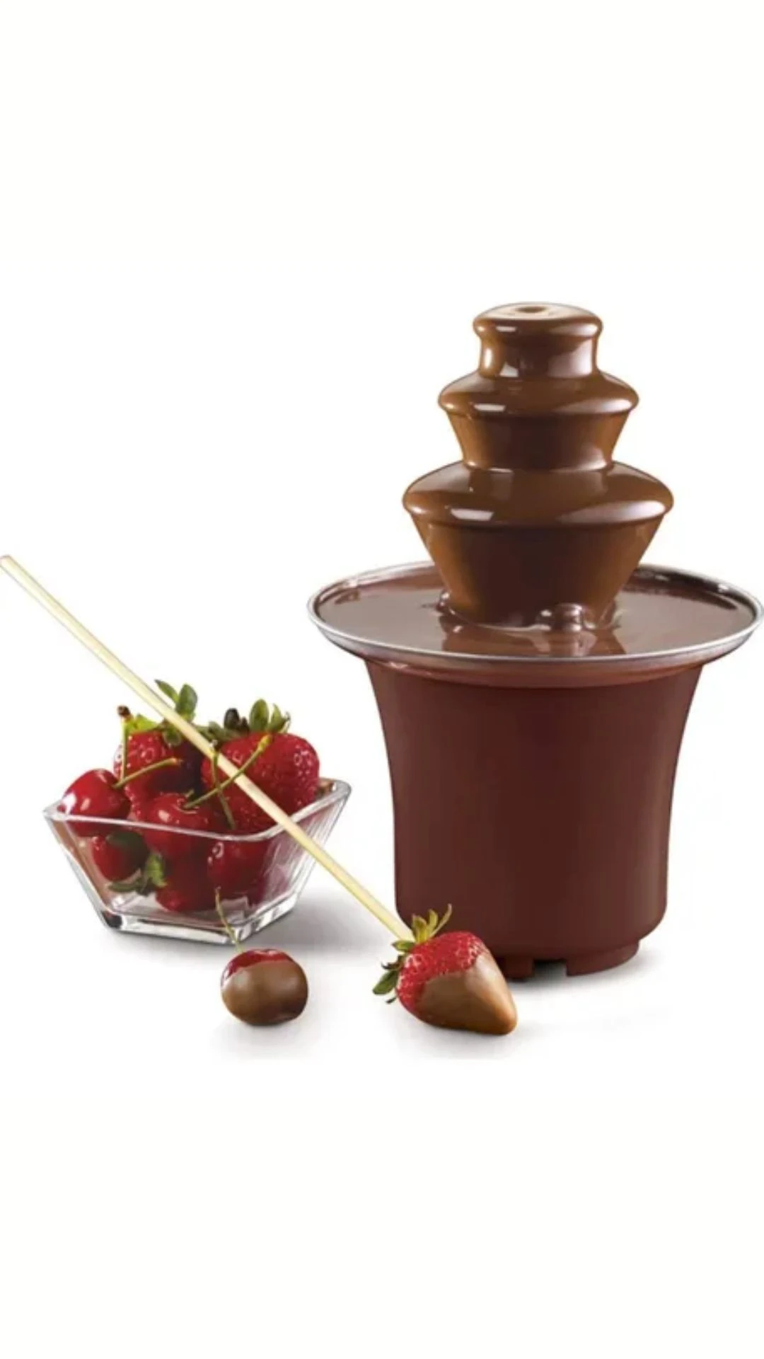 Fuente de chocolate eléctrica mini con cascada continua, color marrón oscuro, en uso con fresas y palillos de madera sobre fondo blanco.