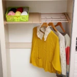 Repisa expandible en madera clara con cesta verde y ropa colgada, ideal para organizar armarios sin obras.