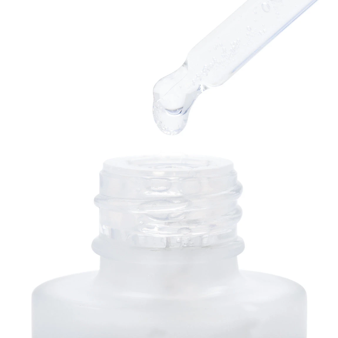 Dropper de vidrio con gota de suero transparente sobre boca de frasco blanco, mostrando textura líquida y aplicación directa para rostro.
