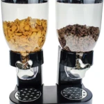 Dispensador de cereales de dos compartimentos con tapas negras y dispensadores metálicos, conteniendo maíz y hojuelas de chocolate.