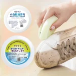 Mano aplicando crema blanca sobre punta de tenis sucio; envases redondos con etiquetas en coreano, chino y japonés visibles.