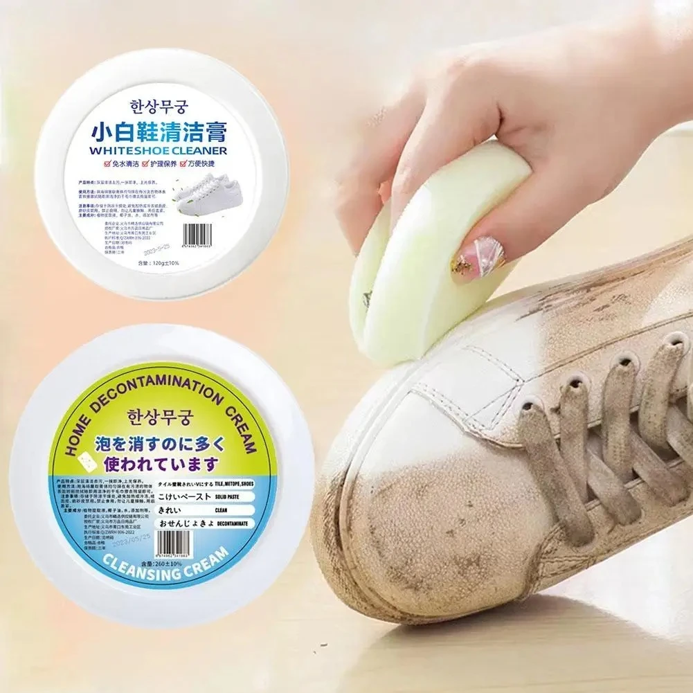 Mano aplicando crema blanca sobre punta de tenis sucio; envases redondos con etiquetas en coreano, chino y japonés visibles.