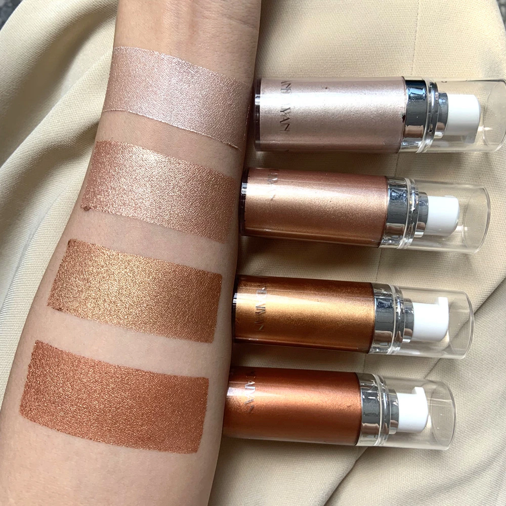 Cuatro iluminadores corporales Shimer en tonos dorados y bronce con acabado brillante, aplicados en el antebrazo junto a sus envases cilíndricos de cristal y metal.
