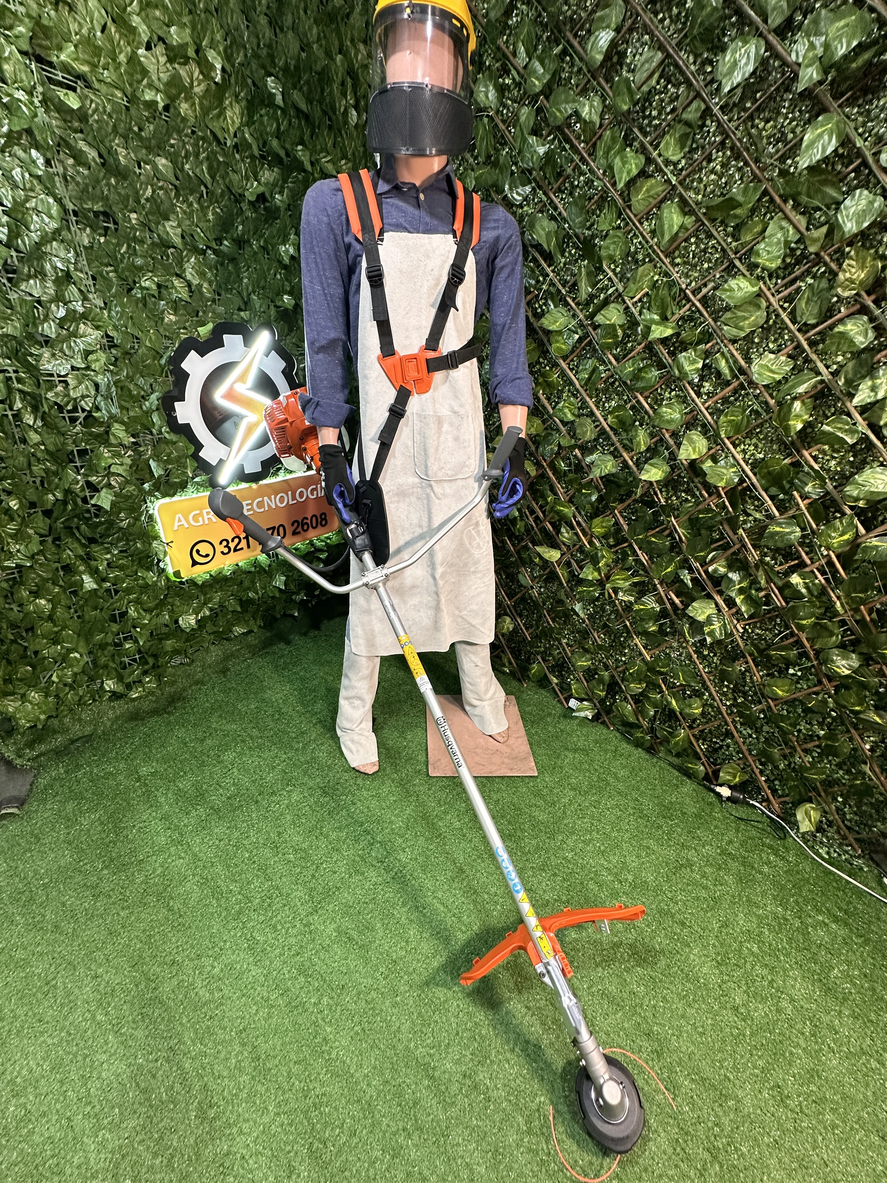 Maniquí con kit de protección integral para carnaza, incluyendo delantal blanco, arnés naranja y guantes azules, sobre fondo de enredadera verde.