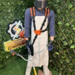 Maniquí con kit de protección integral para carnaza, incluyendo delantal beige, arnés naranja, casco amarillo con visera y guantes azules, sobre fondo de vegetación artificial.