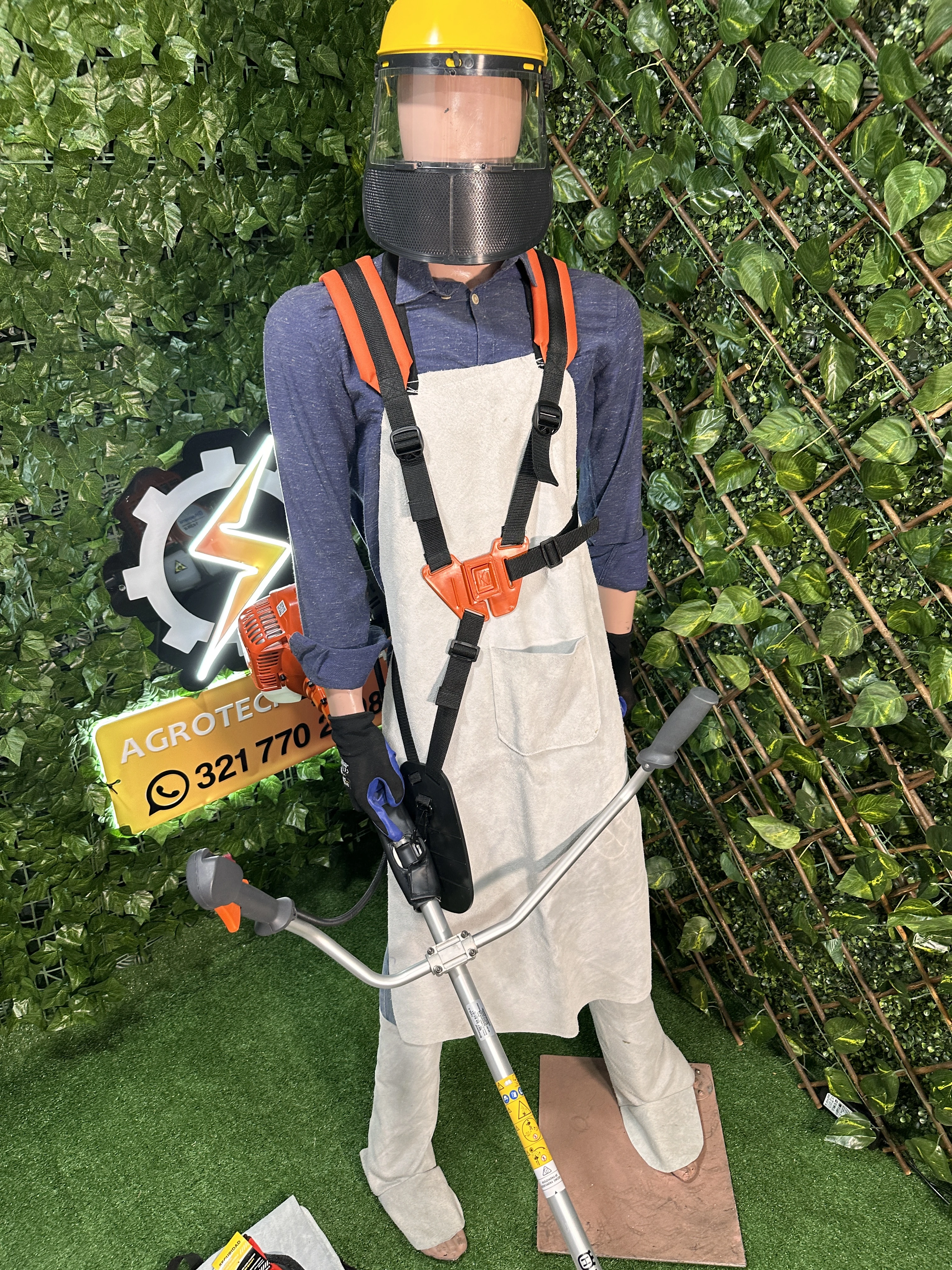Maniquí con kit de protección integral para carnaza, incluye delantal beige con arnés naranja y casco amarillo con visera transparente, sobre fondo verde artificial.
