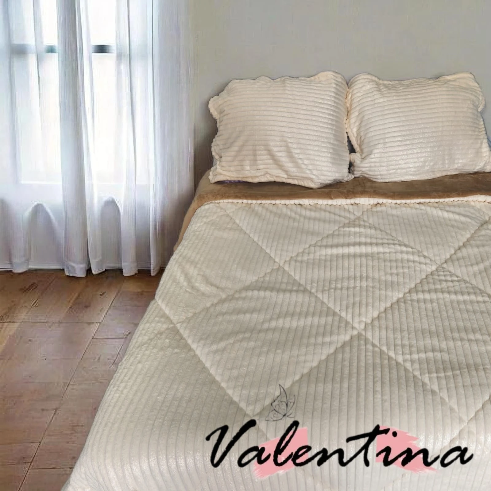 Edredón acanalado color crema con ojero, sobre cama doble con sábanas a juego, en habitación con cortinas blancas y piso de madera.