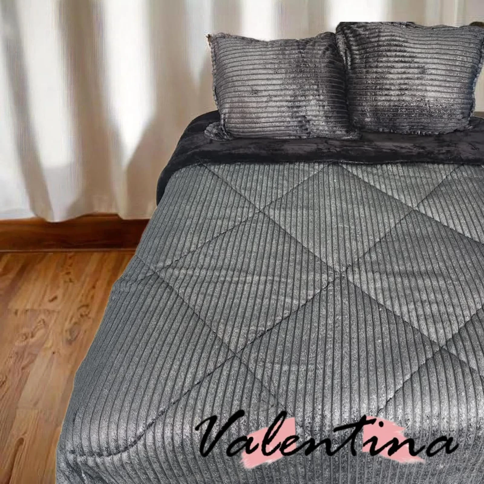 Edredón acanalado gris oscuro con ojero, textura de terciopelo y costuras diagonales, sobre cama doble con cojines a juego.