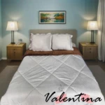 Edredón acanalado blanco con ojero, sobre cama doble con cojines y sábanas marrones, en habitación con lámparas y cuadro decorativo.