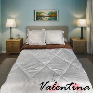 Edredón acanalado blanco con ojero, sobre cama doble con cojines y sábanas marrones, en habitación con lámparas y cuadro decorativo.
