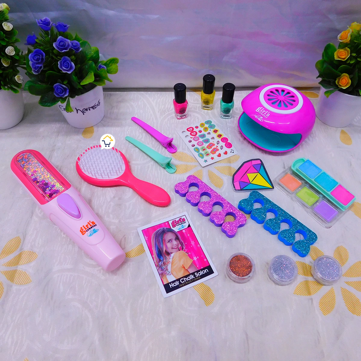 Kit de uñas y secador de pelo mágico para niñas, con esmaltes, pegatinas, cepillo, espejo, paleta de colores y accesorios brillantes sobre tela blanca con flores.