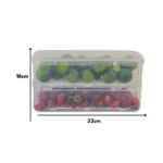 Organizador de nevera transparente con rejilla interna, mostrando limones en la parte superior y fresas en la inferior, con dimensiones de 32 cm de ancho y 16 cm de alto.