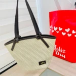 Bolso de mano tejido en yute natural con asas negras y detalle bordado. Ideal para llevar compras frescas de forma sostenible.