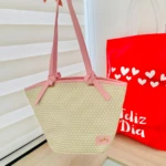 Bolso de mano tejido en yute natural con asas rosas, diseño estructurado y etiqueta visible. Ideal para compras diarias con estilo sostenible.