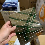 Ducha cuadrada en acero inoxidable sin tubo, con múltiples orificios para chorro uniforme, mostrada en mano sobre cajas de almacenamiento.