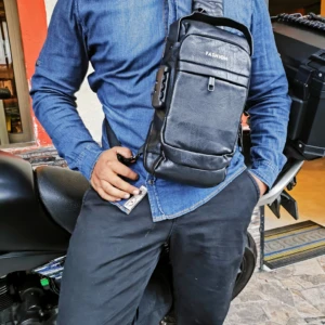 Hombre usando bolso antirrobo de cuero negro con bloqueo y puerto USB, sobre motocicleta.