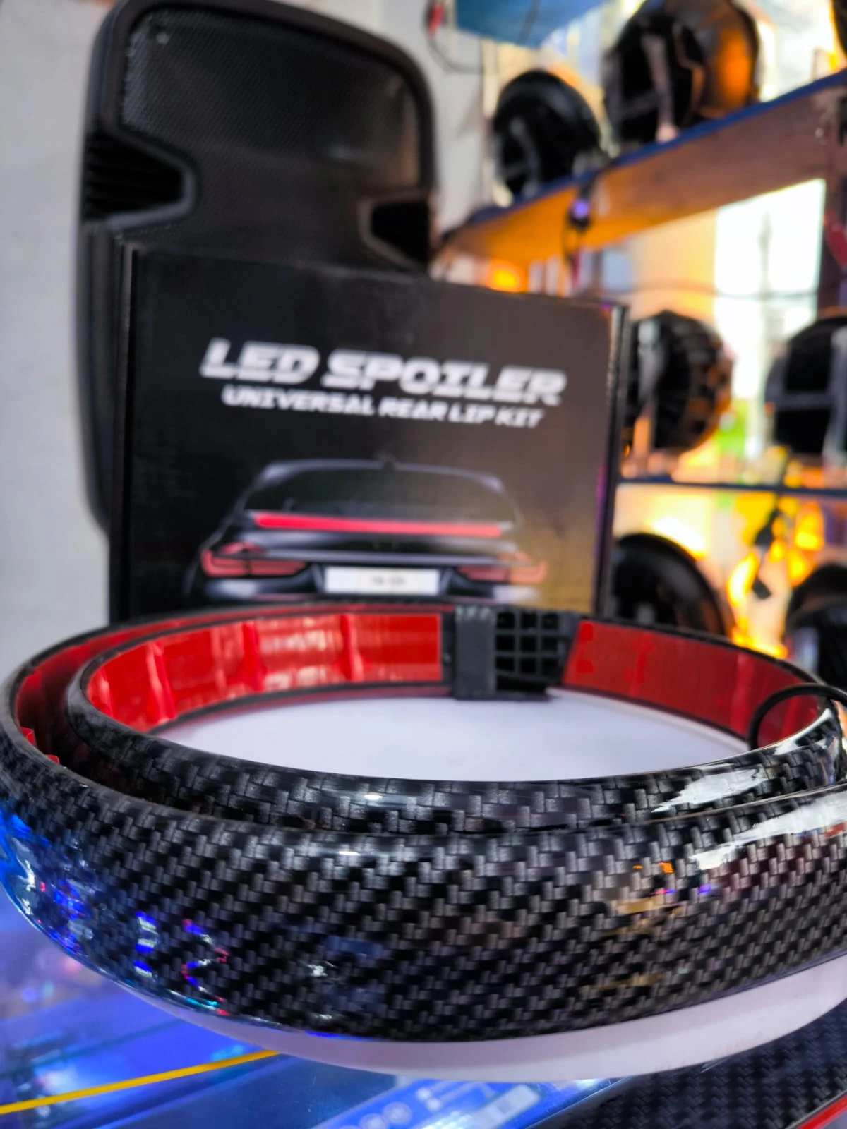 Spoiler de fibra de carbono con luces LED rojas, visible en primer plano sobre su caja negra con del producto.