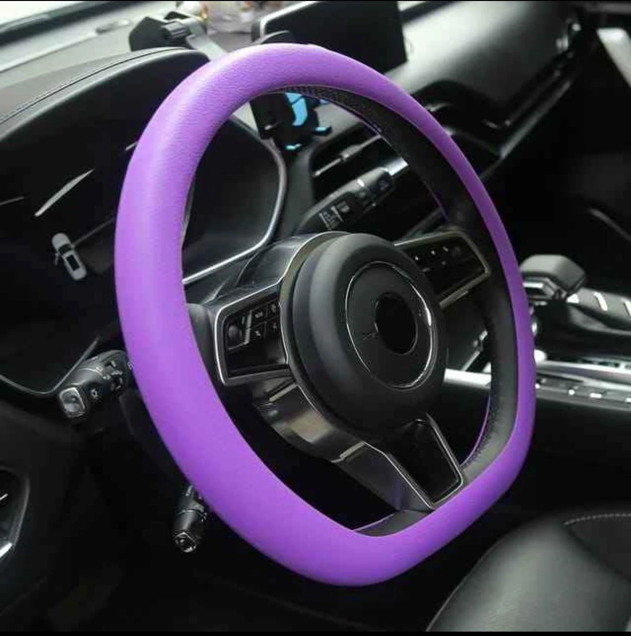 Volante de coche con forro de silicona antideslizante en color morado, instalado en interior de vehículo, mejora el agarre y protege contra el calor.